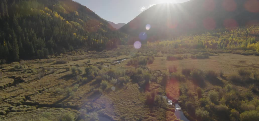 The sun is shining down on a river winding through a mountain valley