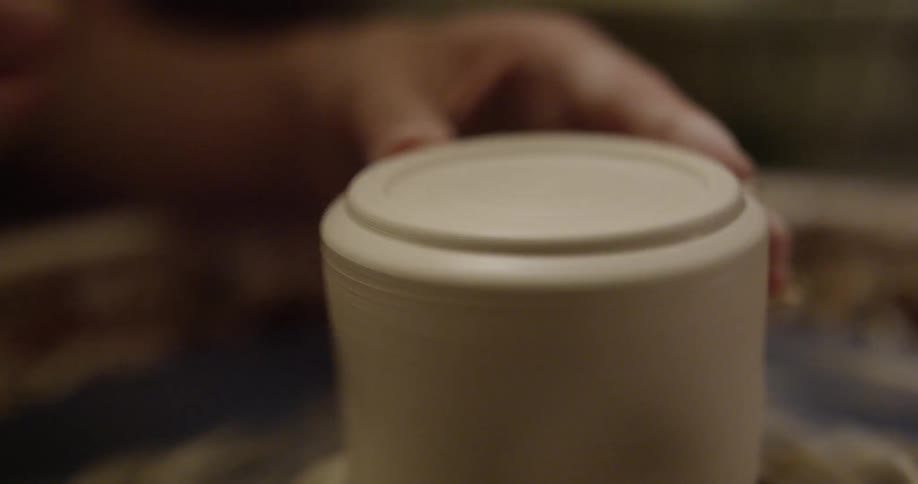 A woman shapes clay on a pottery wheel