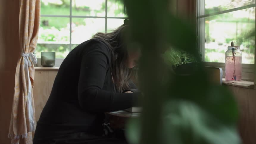 A woman is sitting at a small table drawing in a book