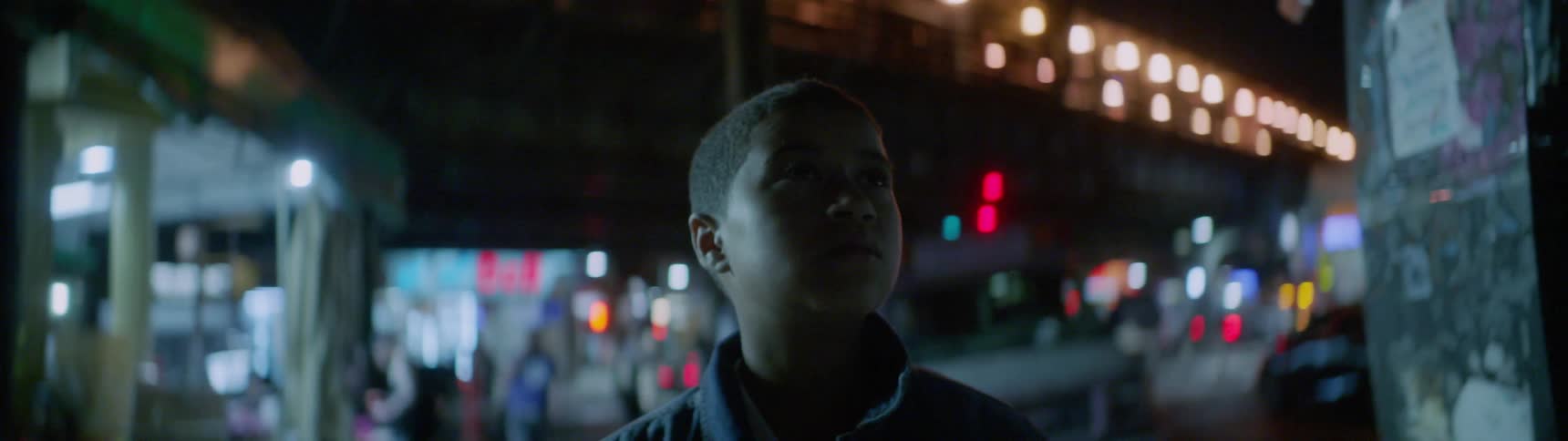 A teenage boy is standing outside in a city at night looking around