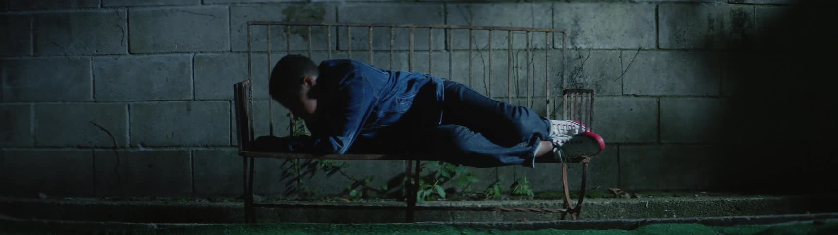 A young man trying to sleep on a metal bench