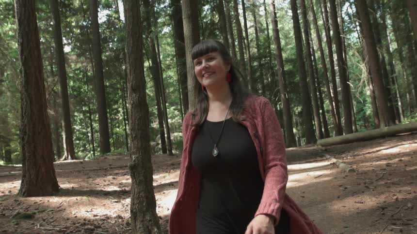 A woman slowly walking and smiling as she travels through the woods down a path