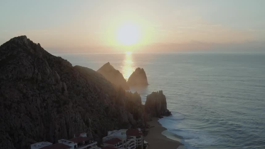 The sun is setting in the ocean near a resort on a beach