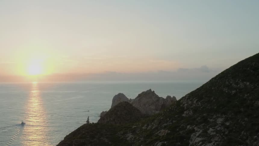 The sun rises over the ocean near a rocky hill