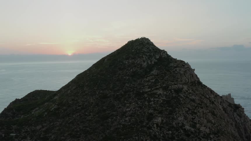 The sun sets behind a coastal mountain peak
