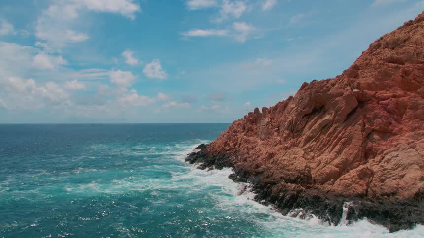 Blue ocean water waves are crashing against the rocks of a island