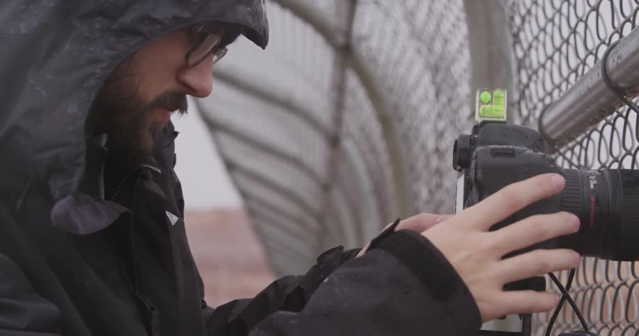 A man takes a photograph through a fence on a rainy day