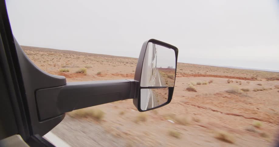 A rearview mirror showing the desert landscape as the vehicle drives down the road