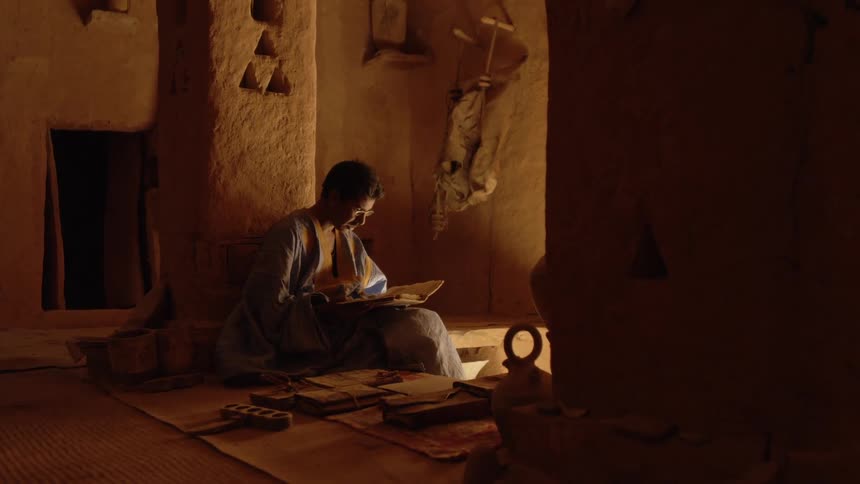 A man sits in his home and picks up a book to read