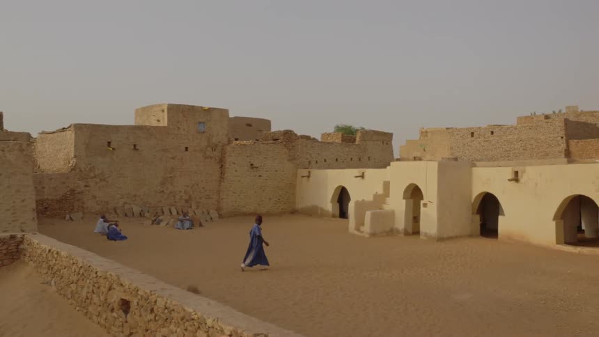 A man is walking through a village in northern africa at sunset