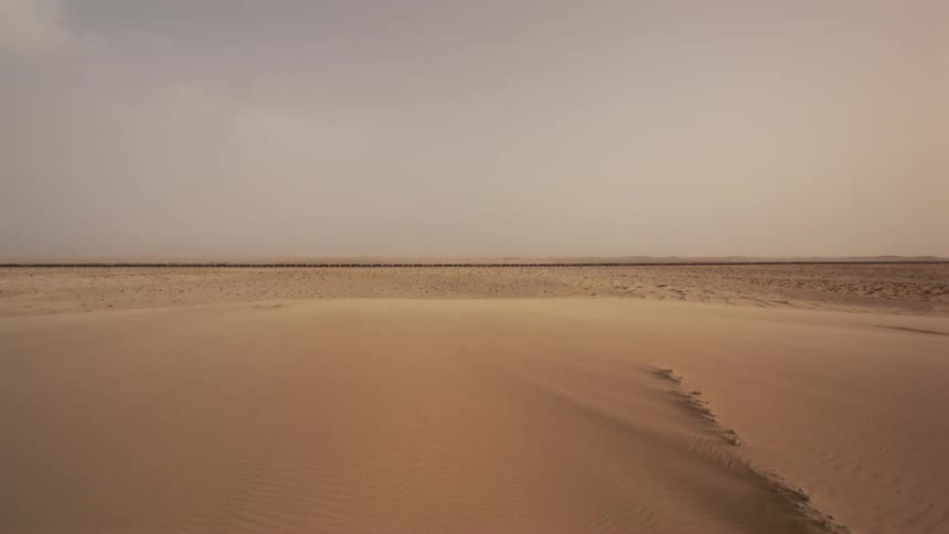 Sand covers a desert landscape at sunset