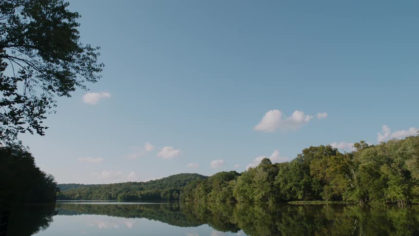 Trees and sky are reflected on the lake surface on a sunny day