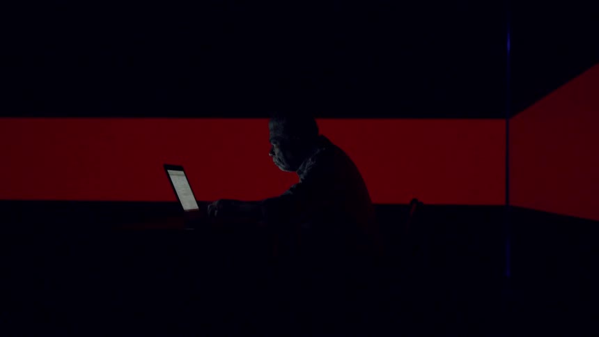 Man types on a laptop with lights flashing around him
