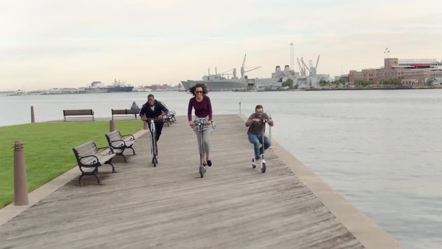 Friends ride scooters on a pier at sunset
