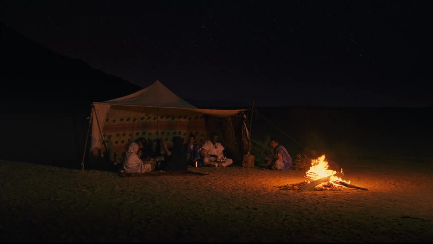 People sit in a tent in front of a fire