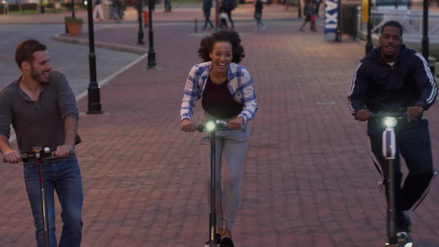 A trio of people riding scooters over a brick walkway