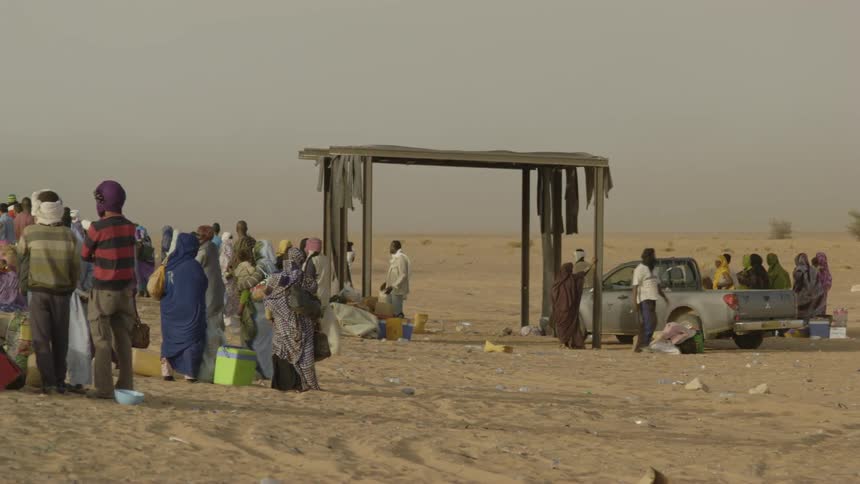 Many people are standing in the desert waiting for the train