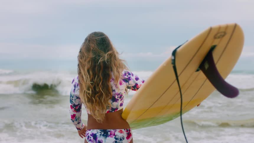A woman carries a surfboard towards the ocean