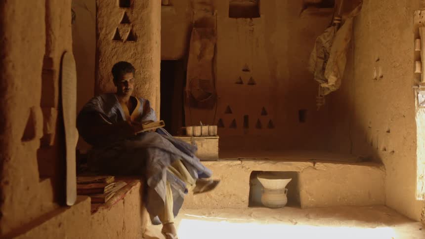 A man enters an adobe type house and sits down to read