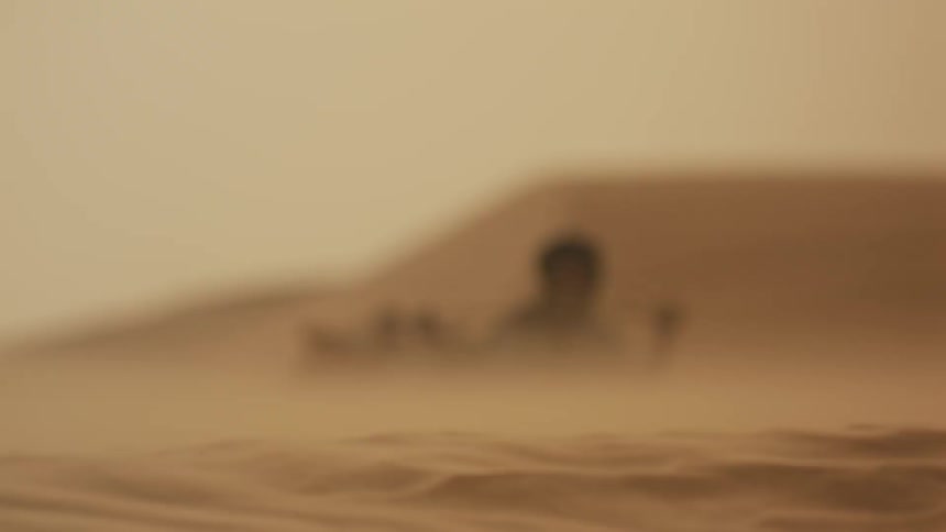An old man is leading a group of bedouin through the desert on a windy day