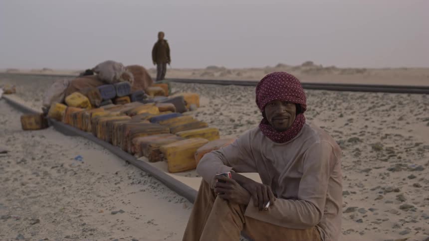 Man smokes a cigarette while sitting next to a train track in the desert