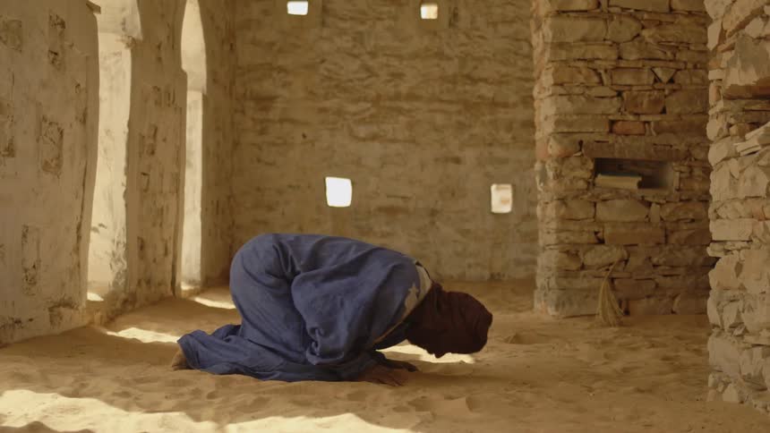 An african man is kneeling down for prayer inside a mosque during the day
