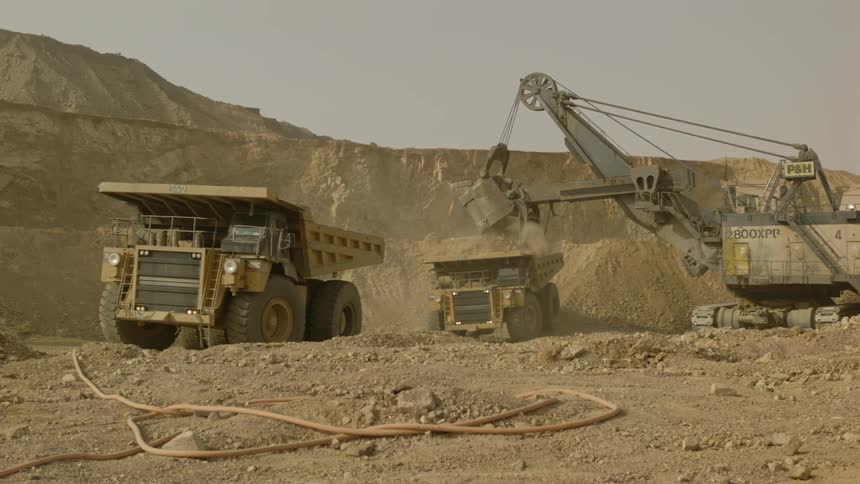 Heavy equipment dropping into a dump truck before it starts to pull away