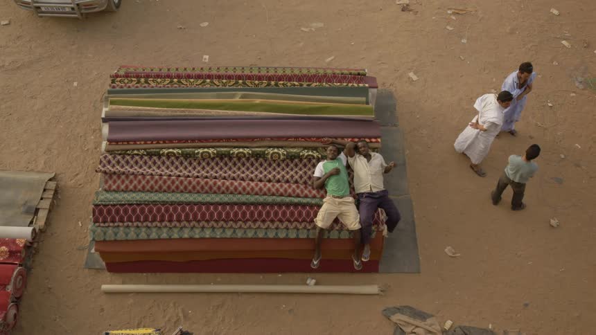 Men rest while others talk near piles of fabric outside during the day
