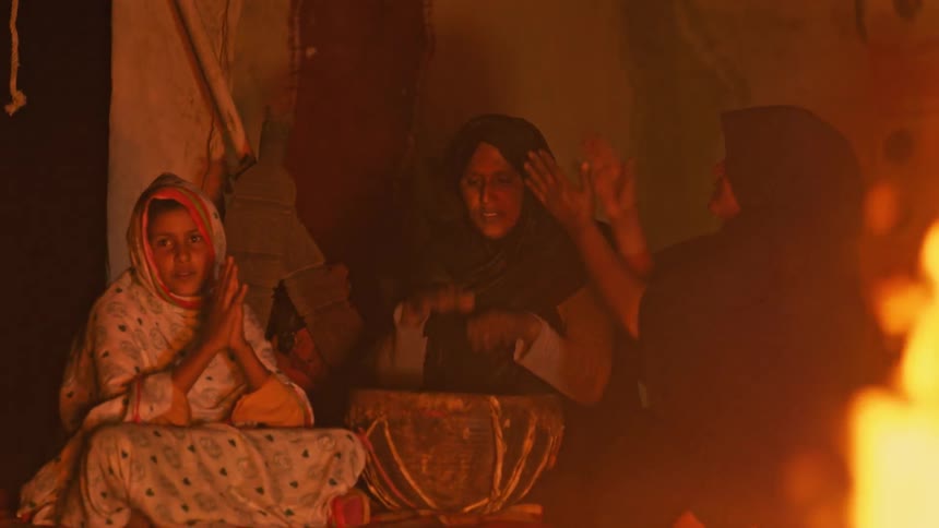 Women sing and clap while sitting next to a fire