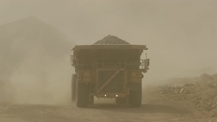 A dump truck hauls dirt from a dusty area