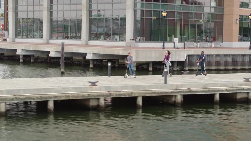 People are riding scooters along the wooden pier by the city