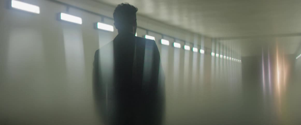 A man walks down a hallway with fluorescent lighting on the walls