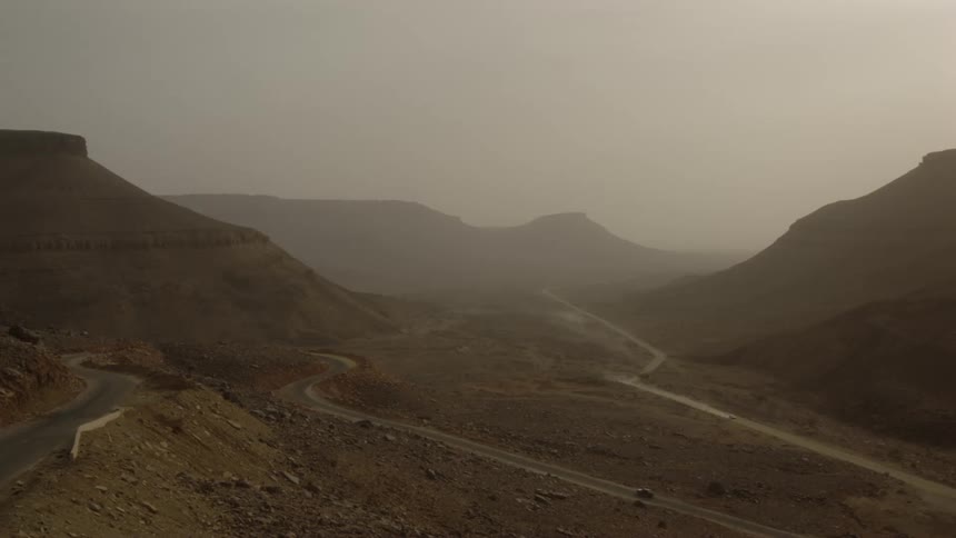 Dust is hanging in the air over two roads in a desert landscape during the day