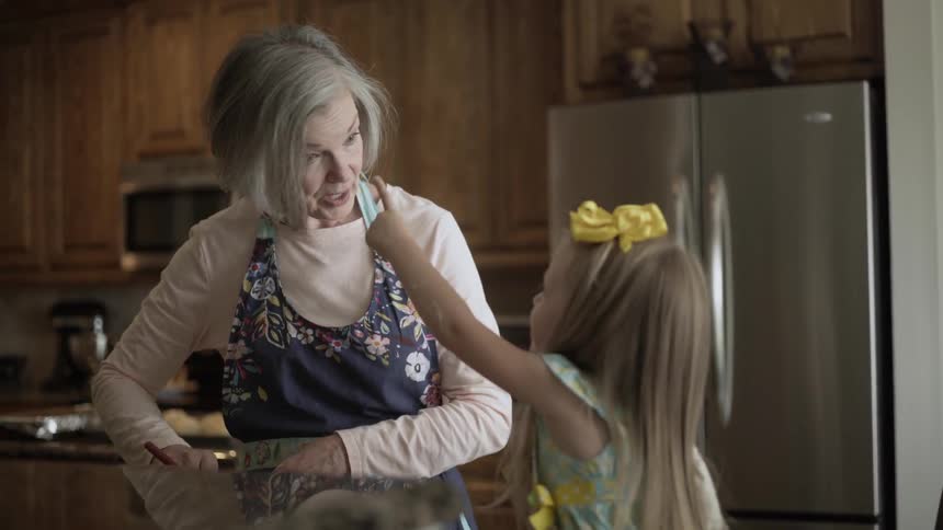 An elderly woman and a girl are baking in a kitchen during the day