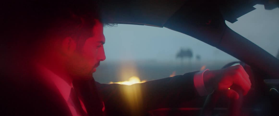 A man sits in a car while a fire burn outside