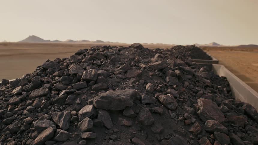 A train hauls iron ore across a desert at sunset