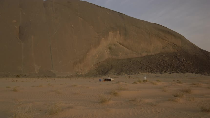 Man walks toward a tent at the base of a tall rocky hill