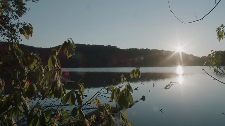 The lake surface reflects the surrounding trees on a sunny day