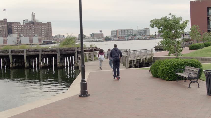 Three friends ride scooters across a bridge near the city pier