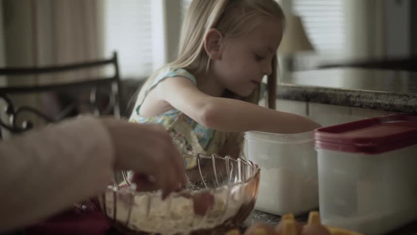 Woman and girl add flour to a bowl while baking