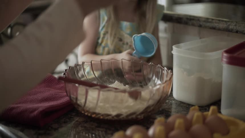 A young girl adds flour to a bowl