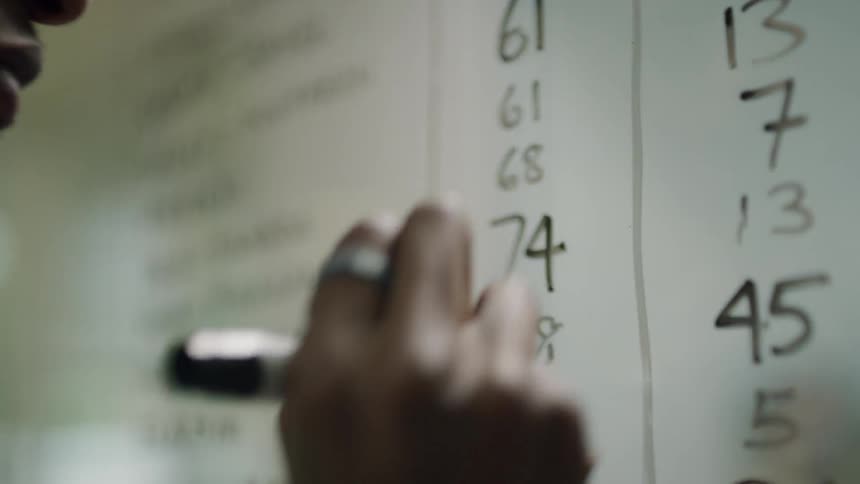 Man writes numbers on a clear dry erase board