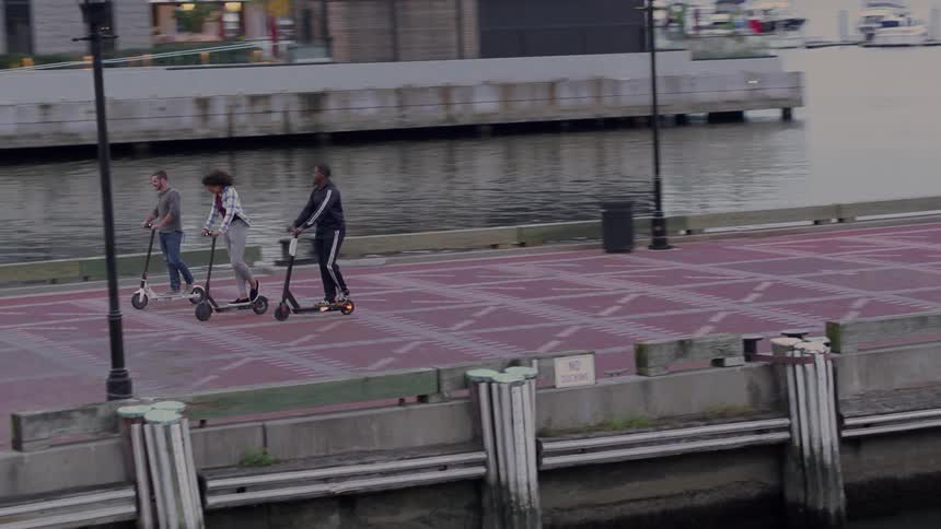 Three friends are riding scooters on a pier at dusk