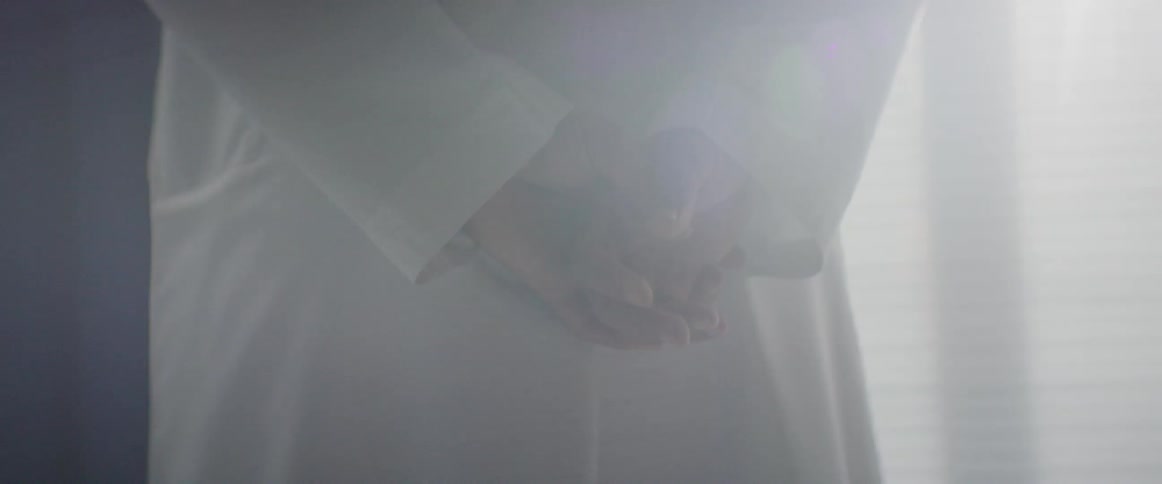 A man wearing a white robe has his hands clasped behind his back