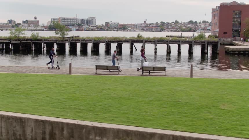 Friends ride scooters along a pier