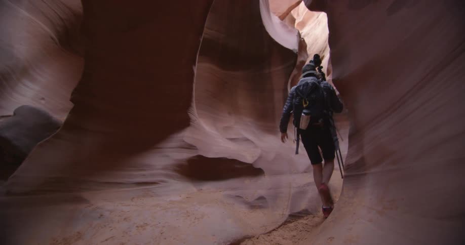 A photographer hikes through a cave with a tripod and camera