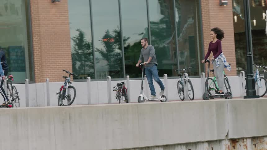 Friends are riding scooters through a city during the day