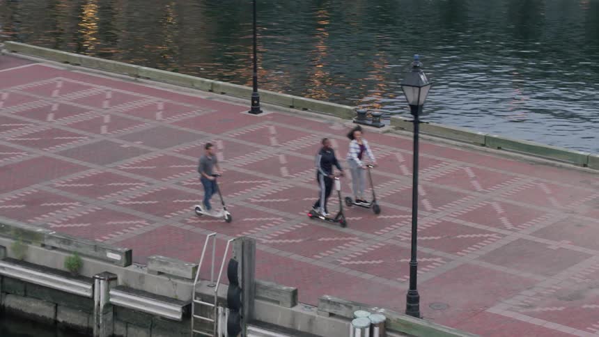Three people are riding scooters down a pier
