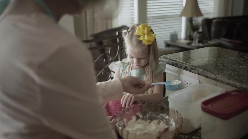A girl pours flour into a bowl helping her grandmother