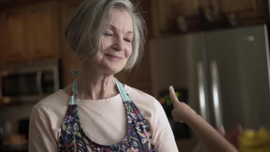 An older woman smiles as she interacts with a child in a kitchen during the day